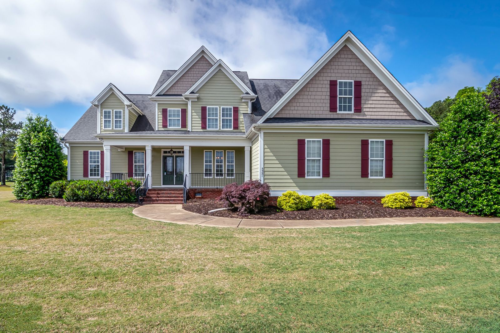 Full front of a welcoming home with maroon shutters, a covered porch, and a lawn